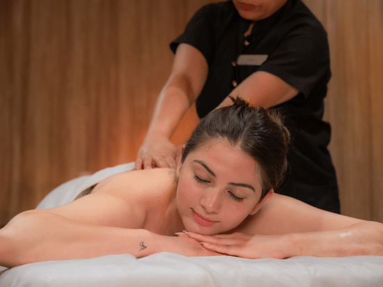 A women lying on her stomach and receiving back massage by a masseuse wearing a black uniform at The Manor Luxury Apartments, Shimla.